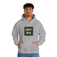 Person wearing a Heavy Blend Hoodie Gildan 18500 Unisex Jersey with big USYGO logo on the front. Made from 50% Cotton 50% Polyester in Sport Grey. Pouch pocket and the tear-away label make for a highly comfortable, scratch-free wearing.