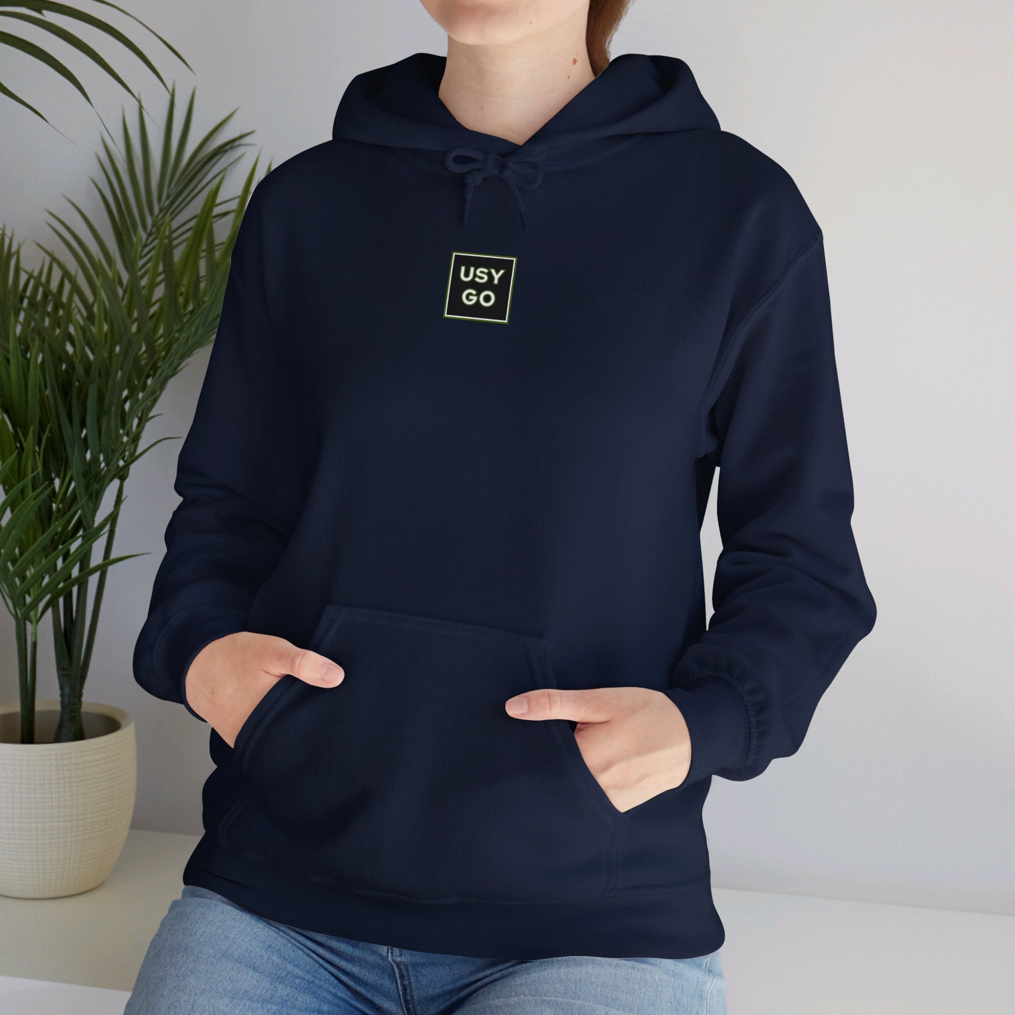 Person wearing a Heavy Blend Hoodie Gildan 18500 Unisex Jersey with USYGO logo on the front. Made from 50% Cotton 50% Polyester in Navy. Pouch pocket and the tear-away label make for a highly comfortable, scratch-free wearing.