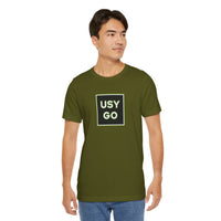 Person wearing a T-Shirt Bella+Canvas 3001 Unisex Jersey Short Sleeve Tee with USYGO logo on the front. Made from lightweight 100% Airlume combed and ring-spun cotton in Olive, ideal for active and leisure wear.